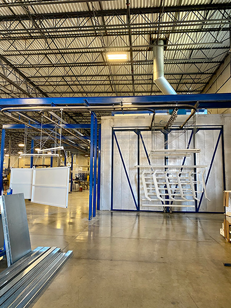 RTT Finishing Solutions powder coating line featuring an overhead conveyor system, large curing oven, and suspended metal components inside a manufacturing facility.